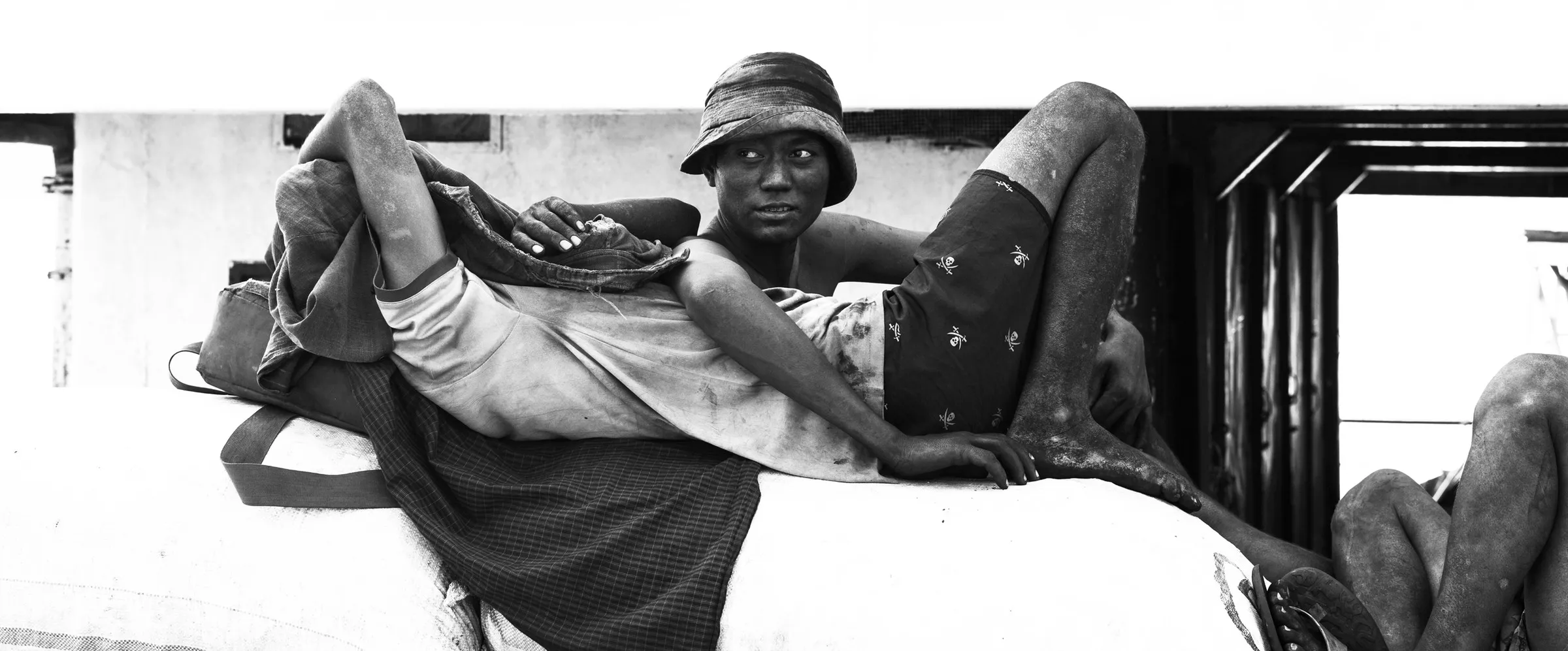 A dock worker reclines across cargo sacks and looks back at the camera