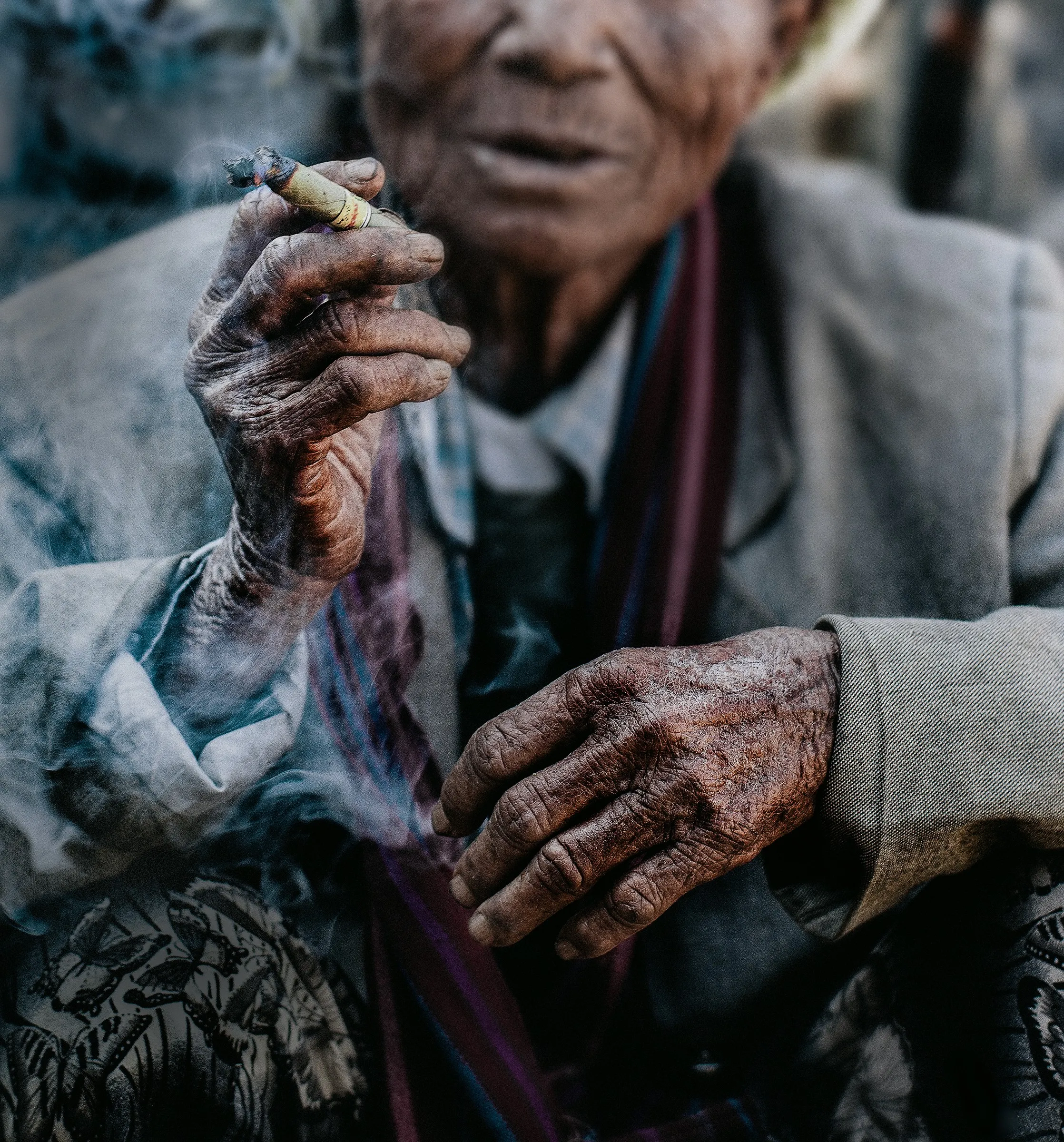 An elderly woman’s worn hands holding a smoking cheroot