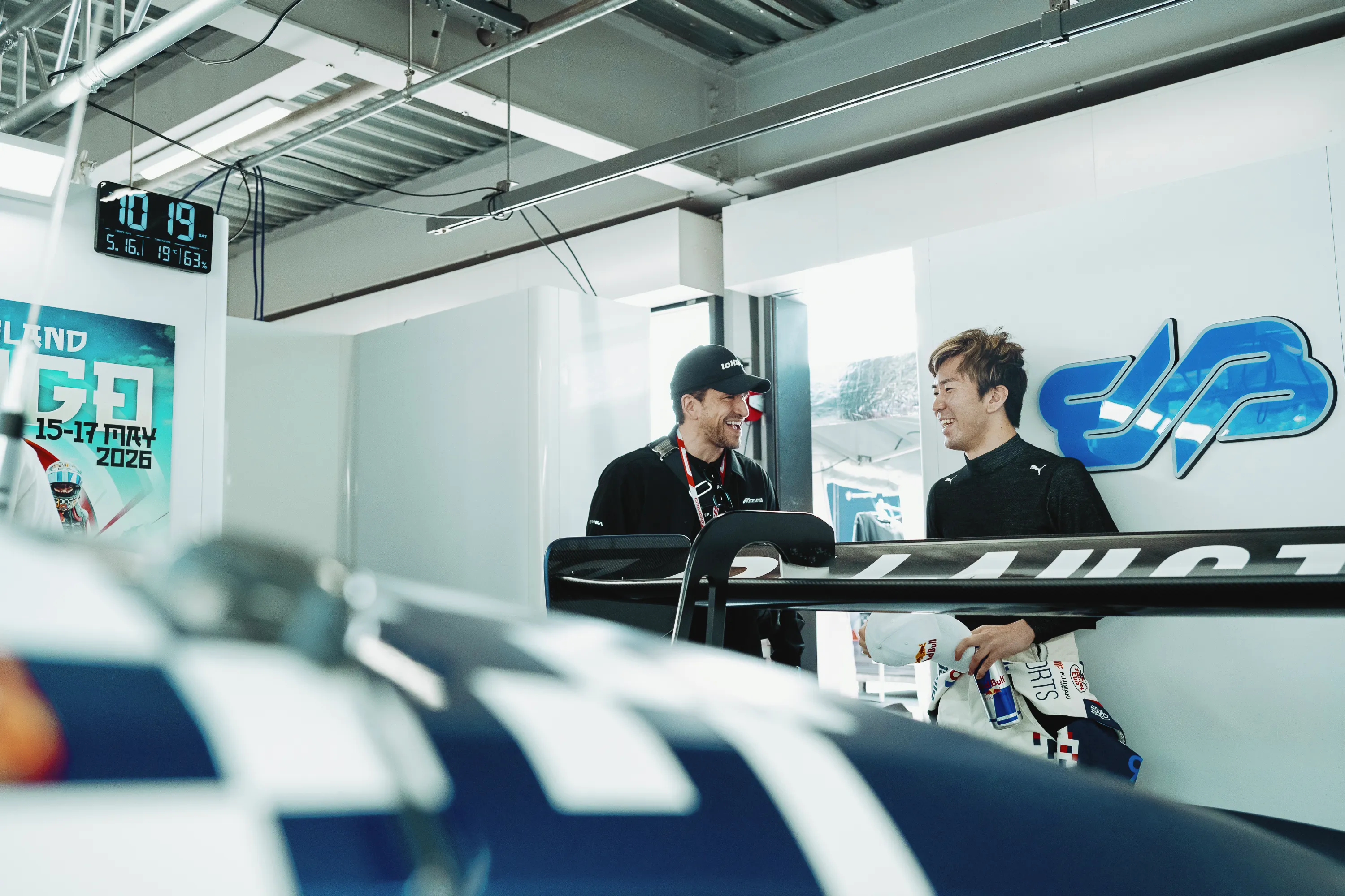 Steven Ilous and driver Ukyo Sasahara laughing in the garage, the car’s rear wing in the foreground